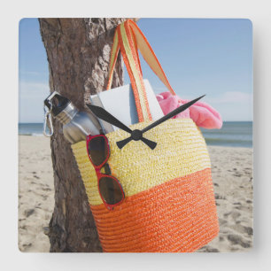 Bag die op boomstam hangt bij zandstrand vierkante klok