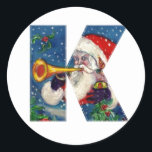 CHRISTMAS K LETTER/SANTA CLAUS BUGLER RONDE STICKER<br><div class="desc">K initiaal Letter-kerstmonogram. Kleurrijk,  wit en artistiek acrylschilderij voor Kerstmis. Santa Claus,  sneeuwwinternacht met bloemige ornamenten,  kat,  rode boog,  groene decoratieve planten,  rode linten,  holbessen,  poppen en speelgoed in de sneeuw door Bulgan Lumini (c) com</div>