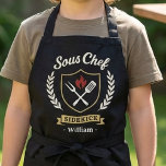 Custom Name Sous Chef Sidekick Child Apron Schort<br><div class="desc">Make kitchen time extra fun with this personalized Sous Chef Sidekick kids apron. Featuring a stylish crest design with cooking utensils, flame detail, and custom name personalization, this apron is perfect for little helpers who love baking, cooking, and BBQ time with family. A great gift for birthdays, holidays, Father’s Day,...</div>