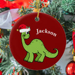 Cute Dinosaur Kerstmis Keramisch Ornament<br><div class="desc">Geweldige groene dinosaurus glimlacht en ziet er erg schattig uit in een feestelijke rode kersthoed. Ik hou van prehistorische kerstdieren en cadeaus waar kinderen van zullen houden. Pas dit geschenk met de naam van de ontvanger aan om het nog meer gepersonaliseerd te maken.</div>