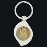 De Geliefden Kussende Omhelzing door Gustav Klimt Sleutelhanger<br><div class="desc">Zonlicht schittert van de wervelende gouden omhelzing die de geliefden omringt in het meesterwerk De Kus van Gustav Klimt. De scène is een paradox van intimiteit en isolement. Het paar staat op een afgrond, een veld van kleurrijke bloemen aan hun voeten, maar ze zijn zich niet bewust van de wereld...</div>