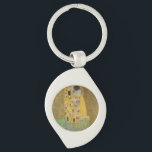 De Geliefden Kussende Omhelzing door Gustav Klimt Sleutelhanger<br><div class="desc">Zonlicht schittert van de wervelende gouden omhelzing die de geliefden omringt in het meesterwerk De Kus van Gustav Klimt. De scène is een paradox van intimiteit en isolement. Het paar staat op een afgrond, een veld van kleurrijke bloemen aan hun voeten, maar ze zijn zich niet bewust van de wereld...</div>