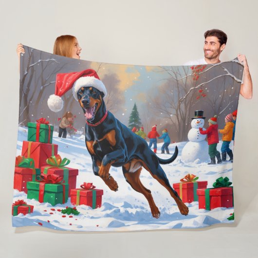 Dobermann loopt in de sneeuw met kerstmuts fleece deken (In situ)