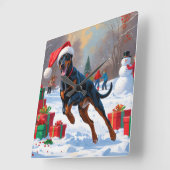 Dobermann loopt in de sneeuw met kerstmuts vierkante klok (Hoek)