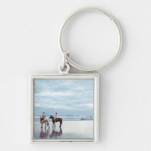 Een paar rijpaarden op het strand van Parkiri in N Sleutelhanger