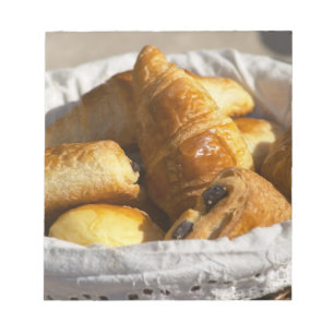 Een rieten ontbijtmand met croissants, en notitieblok