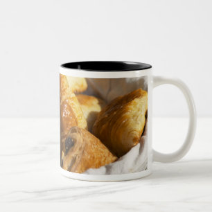 Een rieten ontbijtmand met croissants, en tweekleurige koffiemok