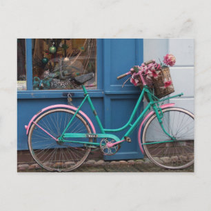 Een roze fiets met een mandje voor teenwilgen en b briefkaart