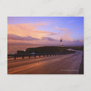 Een weg en een vuurtoren langs de kust op zonsonde briefkaart