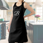 Elegant Wit Custom Monogram op Solid Black Schort<br><div class="desc">Stijlvol zwart schort met gepersonaliseerd monogram. Klassiek donker schort zonder zakken en zonder versieringen anders dan het enkele initiaal gedrukt in kalligrafisch schrift over het bovenste borstgebied. Maakt een eenvoudig maar praktisch accessoire en een elegant gepersonaliseerd cadeau.</div>