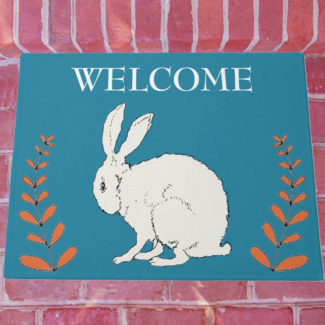 Elegant Zittend Wit Konijn Sinaasappel Planten op  Deurmat (White sitting rabbit with tall orange plants on dark blue Welcome outdoor mat.)