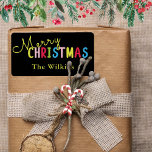 Feestelijke Black Merry Christmas Family Name Desi Etiket<br><div class="desc">Verspreid de feestvreugde met dit feestelijke zwarte vrolijke kerstfeest familienaamontwerp, perfect voor seizoensfeesten. De speelse tekst bevat een levendige mix van gele, roze, rode, groene en blauwe letters, met een klassieke gele familienaam hieronder voor een persoonlijk tintje. Ideaal voor het labelen van vakantiepassen, feestgunsten of decoraties tijdens feestelijke bijeenkomsten. Personaliseer...</div>