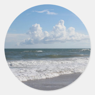Foto van strand met blauwe lucht, dikke wolken en  ronde sticker