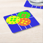 Geel, sinaasappel, & groene pickleballs op blauw h kartonnen onderzetters (Schuin)