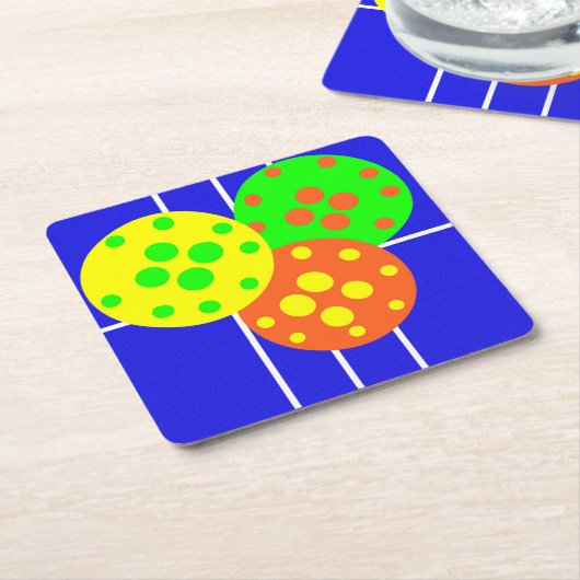 Geel, sinaasappel, & groene pickleballs op blauw h kartonnen onderzetters (Schuin)