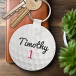 Golf Ball Dimples met zwarte naam rood nummer Sleutelhanger<br><div class="desc">Een sportief en mannelijk patroon voor de jongens en jongens in je familie. Dit sportontwerp is perfect voor elke atleet. Het ziet eruit als een foto van een gouden bal. U kunt dit gebruiken als een Happy Birthday gunst en het aantal jaren omvatten oud in het aantalgebied.</div>
