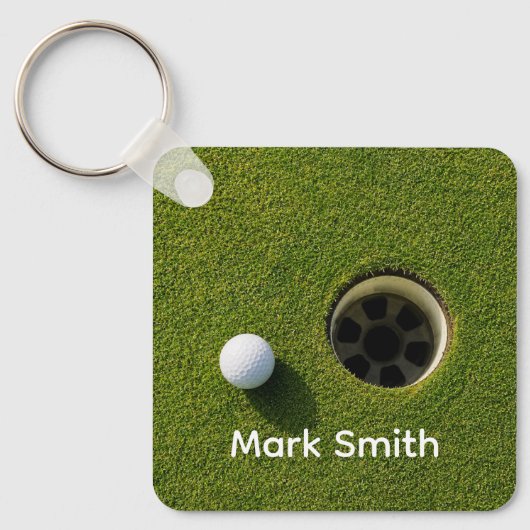 Golfbal naast hole op groene gras golfbaan sleutelhanger (Voorkant)