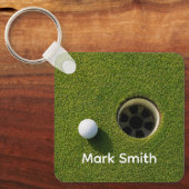 Golfbal naast hole op groene gras golfbaan sleutelhanger (Voorkant)