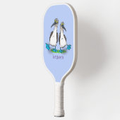 Grappig, gelukkig blauw gefundeerde cartoon die op pickleball paddle (Links)