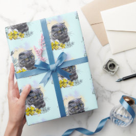 Hand die een grappige zwarte britse kat met bloeme cadeaupapier