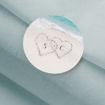 Harten op de zandstrandbruiloft ronde sticker<br><div class="desc">Met twee harten in het zand en de initialen van de bruid en de bruidegom met turkooiswater en witte zandstrandachtergrond,  geweldig voor zomersstrand bruiloft of tropische bestemmingsuithuwelijken.</div>