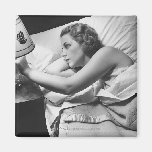 Jonge vrouw liggend op bed die lamp afzetten magneet (Voorkant)