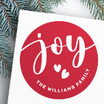 Joy schattige script typografie rode naam kerst ronde sticker<br><div class="desc">Kerstvakantie stickers met het woord "joy" in een elegant wit script over een rode achtergrond met twee harten en jouw naam hieronder. Alle kleuren zijn aanpasbaar in de ontwerptool.</div>