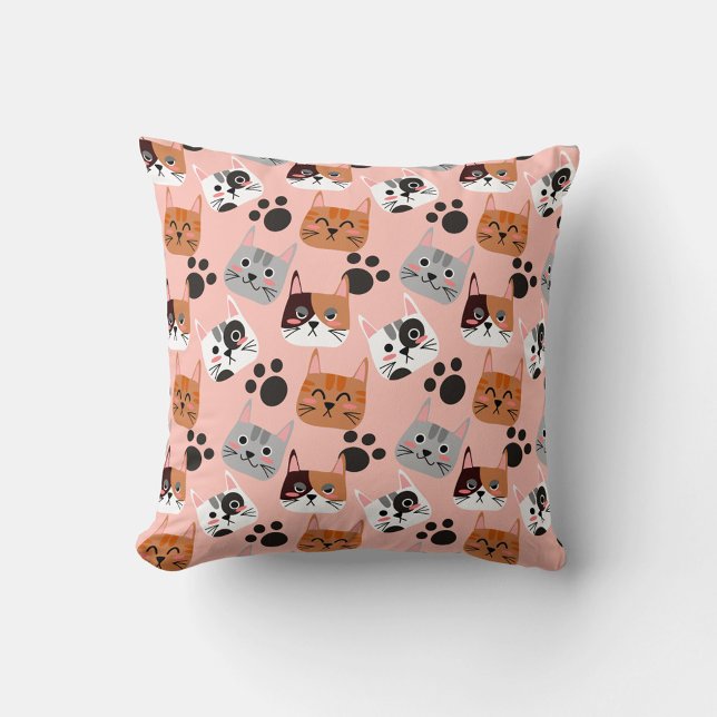 Kat faces kussen (A flat lay shot shows a square pillow with a pink background and a repeating pattern of cartoon cat.)