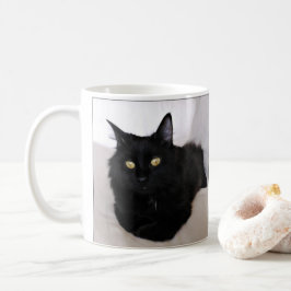 Langwerpige zwarte kat die op de bank ligt koffiemok