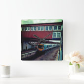 Lichtblauwe trein, onder de brug vierkante klok (Huis)