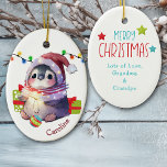 Merry Penguin Kinder keramische keramiek Keramisch Ornament<br><div class="desc">Aan de voorkant van dit keramische siermiddel voor een kind is een schattige baby pinguïn met een kersthoed en een wintersjaal. De pinguïn heeft een kerstboombol tussen zijn voeten en cadeaupakketten ernaast. Er zit een reeks Holiday-lichten achter. De naam van je kind is rood rechts onderaan. De achterkant van de...</div>