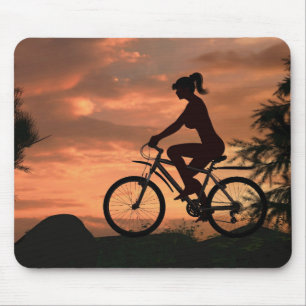 Mooie meid die op haar fiets rijdt bij zonsonderga muismat