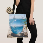 Ocean Reflection in a Lens Ball Tote Bag<br><div class="desc">A sailboat on a sunlit ocean,  its reflection captured in a glass lens ball on beach sand next to a starfish</div>