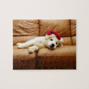 Puppy draagt een pet voor kerstmis en ligt op sofa legpuzzel