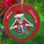 Skelet in Pine Christmas Wreath Red Pet Funny Keramisch Ornament<br><div class="desc">Dit hangende keramische ornament heeft een grappig skelet met ornamenten met sneeuwvlokken tot aan zijn ogen die een rode kerstmuts dragen in een groene speldkrans op een dieprode achtergrond. Pas jouw tekst op de achterkant met de en de Merry Christmas op de voorkant met de sjablonen.</div>