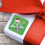 Smiling Christmas Skeleton Ornament Eyes on Green Vierkante Sticker<br><div class="desc">Deze vierkante sticker heeft een lachend skelet met een rode kerstmuts die glanzende ornamenten voor zijn ogen vasthoudt op een groene achtergrond met kleine goudkleurige vlekjes en de tekst Merry Christmas in felgoud.</div>