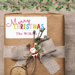 Speelse Witte Vrolijke Kerstmis Familienaam Ontwer Etiket<br><div class="desc">Voeg een feestelijk tintje toe met dit speelse witte vrolijke kerstfeest familienaamontwerp, perfect voor vakantiefeesten. De vrolijke tekst bevat een levendige mix van rode, gele, roze, groene en blauwe letters, met een klassieke rode familienaam hieronder voor een persoonlijke flair. Ideaal voor het labelen van vakantiepassen, feestgunsten of decoraties tijdens feestelijke...</div>
