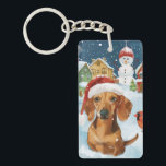 Teckel Winter Wonderland Christmas Joy Sleutelhanger<br><div class="desc">Dit feestelijke ontwerp vangt de vrolijke sfeer van het vakantieseizoen, met een schattige pup die een kerstmuts draagt. De hond is genesteld in een winterwonderland, compleet met een sneeuwpop, een versierde kerstboom en prachtig ingepakte cadeaus. Sneeuwvlokken herfsten zachtjes en voegen een magische toets toe aan het tafereel, terwijl de levendige...</div>