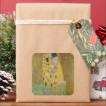 The Lovers Kissingembrace by Gustav Klimt Vierkante Sticker<br><div class="desc">Het zonlicht schittert door de wervelende gouden omhelzing die de geliefden omringt in Gustav Klimts meesterwerk, The Kiss. De scène is een paradox van intimiteit en isolatie. Het paar staat op een afgrond, een veld van kleurrijke bloemen aan hun voeten, maar ze zijn zich niet bewust van de wereld om...</div>