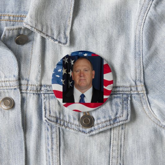 Tom Homan Button with flag waving behind (In situ)