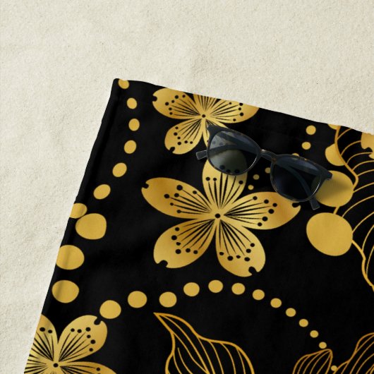 tropische bladeren en bloemen in goud op zwart strandlaken (In situ)