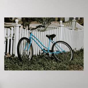 Turquoise fiets leunend tegen een witte schutting poster