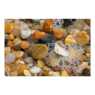 Veel tumbled rotsen op een zandstrand met water perfect poster