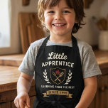 Vintage Barbecue Chef Apron Kids Apprentice Schort<br><div class="desc">Embrace your culinary journey with the "Little Apprentice" apron, a design that blends vintage charm with modern grilling spirit. This graphic apron showcases a sophisticated emblem with a shield, featuring iconic barbecue tools and a fiery emblem, all encircled by elegant laurel branches. The phrase "Learning from the Best Since 1998"...</div>