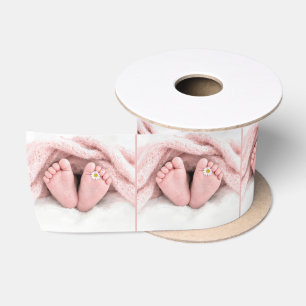 Voetjes van een babymeisje met een witte madeliefj satijnen lint