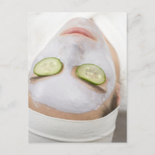 Vrouw met gezichtsmasker en komkommerplakken op briefkaart