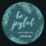 Wees blij Kerst sticker | Sneeuw en pijnbomen<br><div class="desc">Met de hand getekende dennentakken in zachte groene waterverf,  in combinatie met een kalligrafische "wees blij" typografie tegen een getextureerde donkerblauwe achtergrond,  maken een helder en modern vakantiemodel mogelijk.</div>