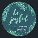 Wees blij Kerst sticker | Sneeuw en pijnbomen<br><div class="desc">Met de hand getekende dennentakken in zachte groene waterverf,  in combinatie met een kalligrafische "wees blij" typografie tegen een getextureerde donkerblauwe achtergrond,  maken een helder en modern vakantiemodel mogelijk.</div>