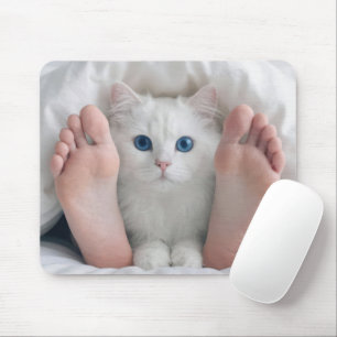Witte kat en menselijke voeten onder een dekbed muismat
